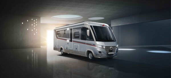 Ein modernes, silbernes integriertes Wohnmobil mit roten und schwarzen Akzenten steht unter runden Oberlichtern, beleuchtet von sanftem Sonnenlicht, das durch eine Tür in einen schlichten, minimalistischen Raum fällt.