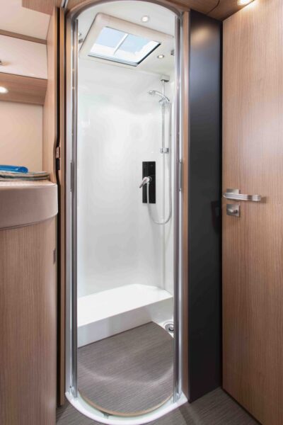 Eine moderne, kompakte Duschkabine mit Glastür in einem holzgetäfelten Bad, mit Handbrause und Oberlicht darüber, in einem integrierten Wohnmobil oder Camper für stilvolles und funktionales Reisen.