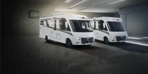 Zwei moderne weiße vollintegrierte Wohnmobile mit schwarzen und goldenen Streifen sind nebeneinander in einer geräumigen, gut beleuchteten Garage mit grauem Betonboden und grauen Wänden geparkt.
