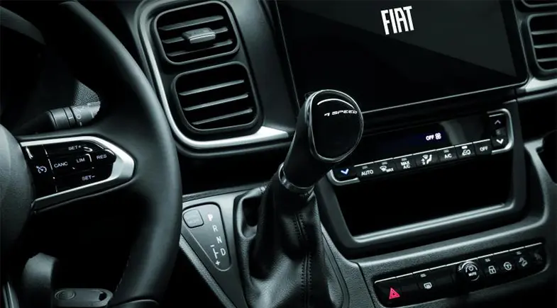 Close-up of a Fiat Ducato motorhome interior with steering wheel, 6-speed automatic transmission, air vents, dashboard controls and a screen with the Fiat logo.