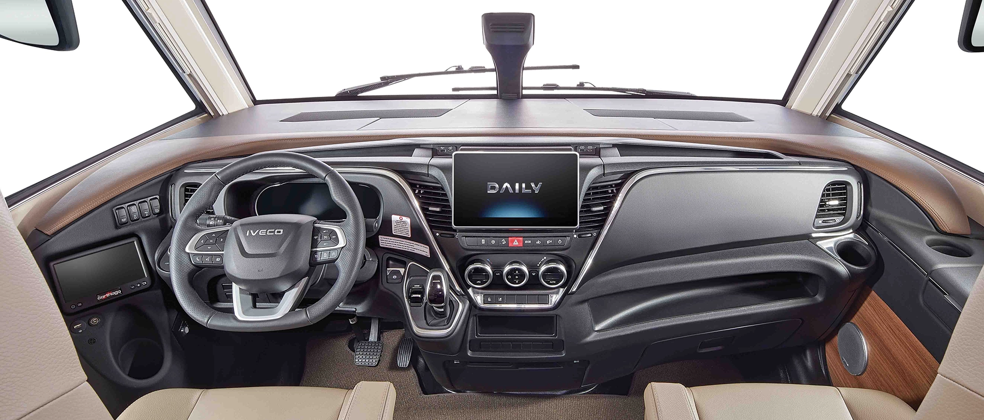 Der Innenraum eines modernen Iveco-Fahrzeugs, das auf einem robusten Fahrgestell für Wohnmobile aufgebaut ist, zeigt ein Lenkrad, ein digitales Armaturenbrett, einen zentralen Touchscreen mit der Anzeige DAILY, Bedientasten und Lüftungsdüsen, alles umgeben von einer eleganten braunen und schwarzen Verkleidung.