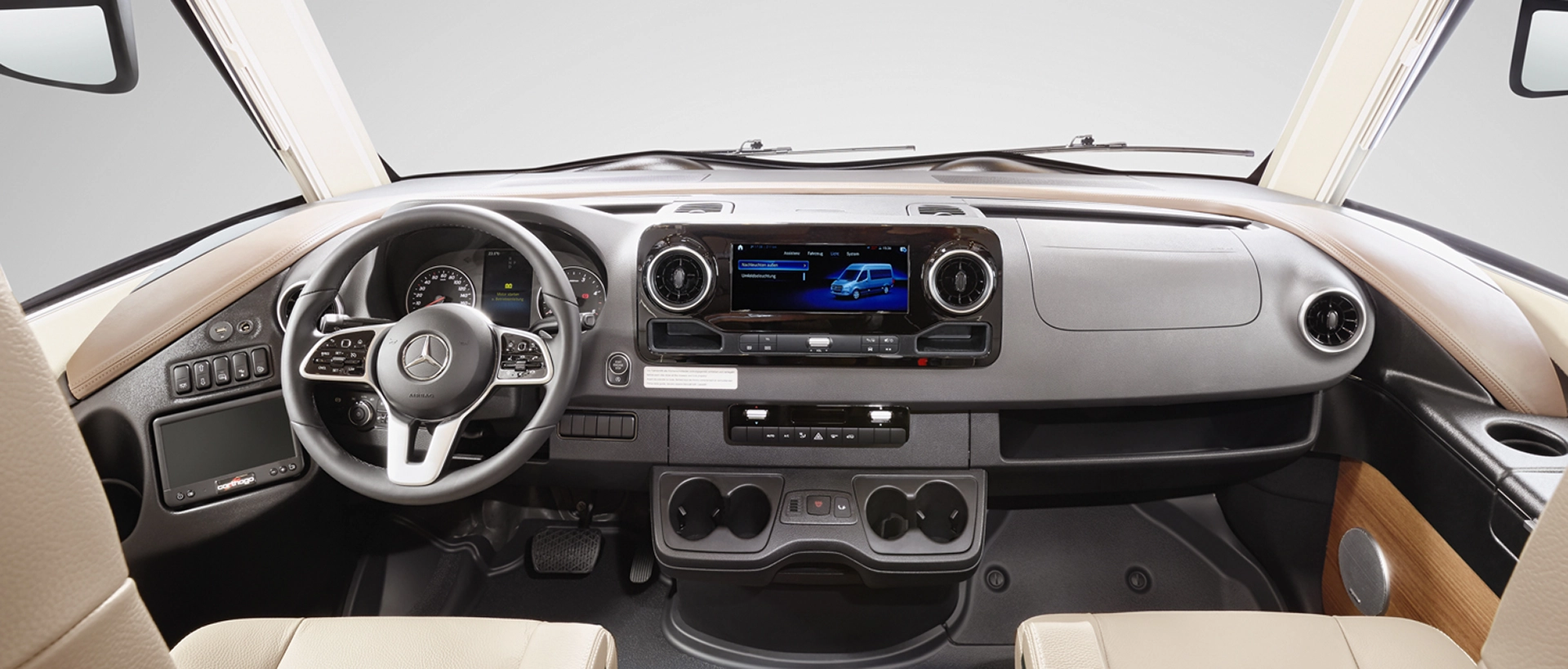 Das Armaturenbrett im Innenraum eines Mercedes-Benz Fahrzeugs mit Lenkrad und Bedienelementen, Digitalanzeige, Lüftungsdüsen, großem Infotainment-Bildschirm und Getränkehaltern - perfekt gestaltet wie das Fahrgestell für Wohnmobile mit eleganten Holz- und Schwarzdekoren.