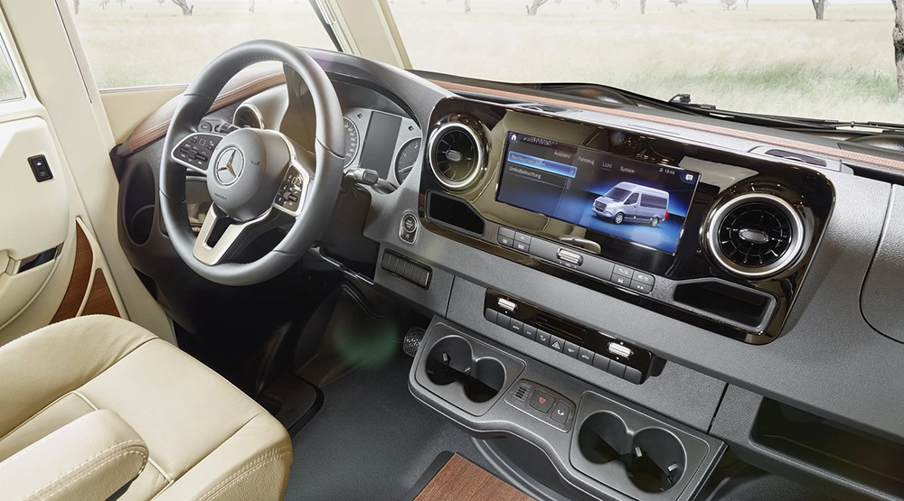 Der Innenraum eines Mercedes-Benz Fahrzeugs zeigt das Lenkrad, die beigen Ledersitze, das Armaturenbrett und den großen Infotainment-Bildschirm mit einem Van-Bild - perfekt für ein mercedes wohnmobil-Abenteuer. Durch die Fenster ist eine grasbewachsene Wiese zu sehen.