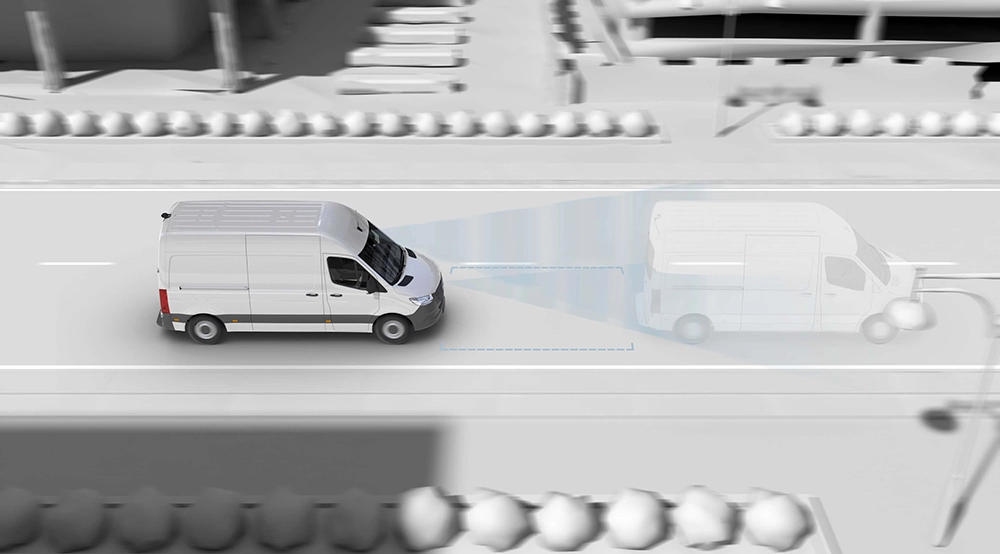 Ein weißes Mercedes Wohnmobil fährt auf einer Stadtstraße, während ein blaues Overlay das fortschrittliche Fahrerassistenzsystem veranschaulicht, das ein vorausfahrendes Fahrzeug erkennt. Im Graustufenhintergrund sind Gebäude, Bäume und Autos zu sehen.