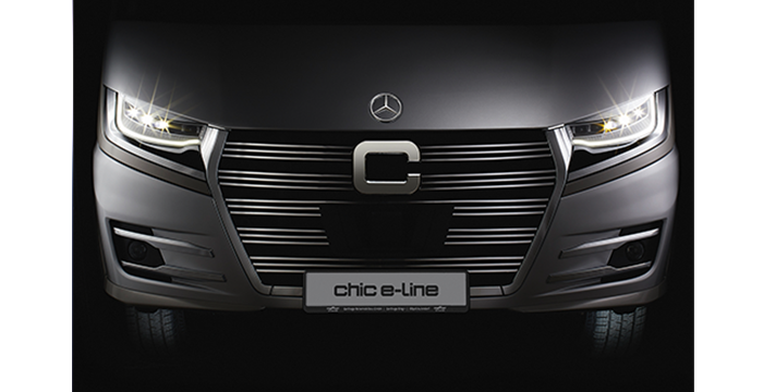 Frontansicht eines schnittigen, modernen Fahrzeugs mit beleuchteten Scheinwerfern, einem markanten Kühlergrill und einem schicken E-Line-Kennzeichen mit dem Mercedes-Benz Logo auf der Motorhaube.