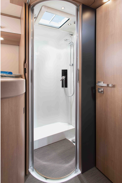Moderne, kompakte Duschkabine in einem holzgetäfelten Carthago C Tourer Wohnmobil-Badezimmer, mit Glastür, Handbrause und Oberlicht, das natürliches Licht hereinlässt.