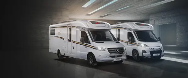 Zwei moderne weiße Wohnmobile mit schwarzen und goldenen Akzenten sind in einer geräumigen, gut beleuchteten Garage mit grauem Interieur geparkt. Beide Fahrzeuge sind mit der Marke "Dethleffs" versehen und haben große Frontfenster.